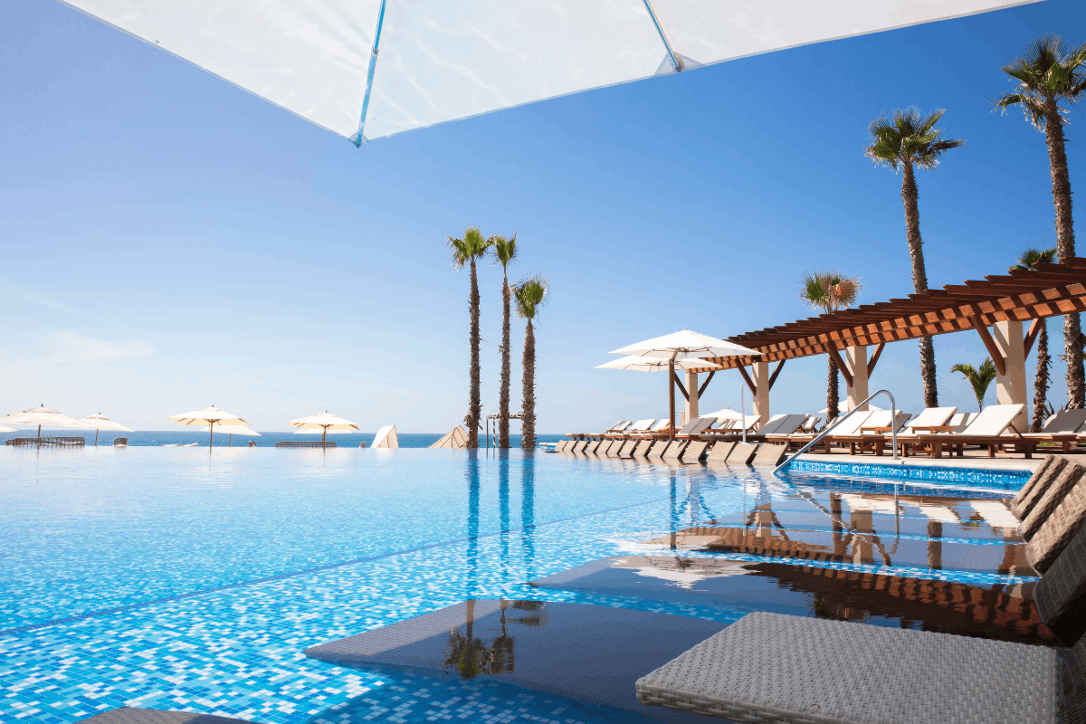 Infinity pool at Krystal Grand Los Cabos with lounge chairs, umbrellas and ocean views.